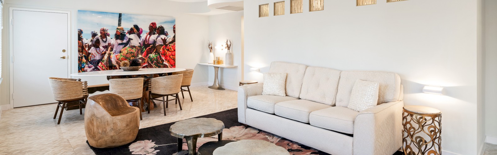A modern living room with a beige sofa, wood tables, art on the wall, and a dining table with chairs. Features a ceiling fan and decor accents.