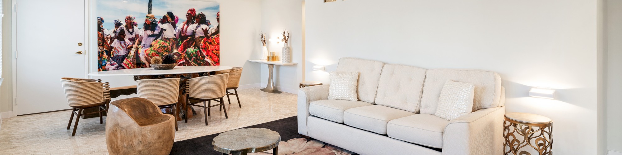 A modern living room with a beige sofa, wood tables, art on the wall, and a dining table with chairs. Features a ceiling fan and decor accents.