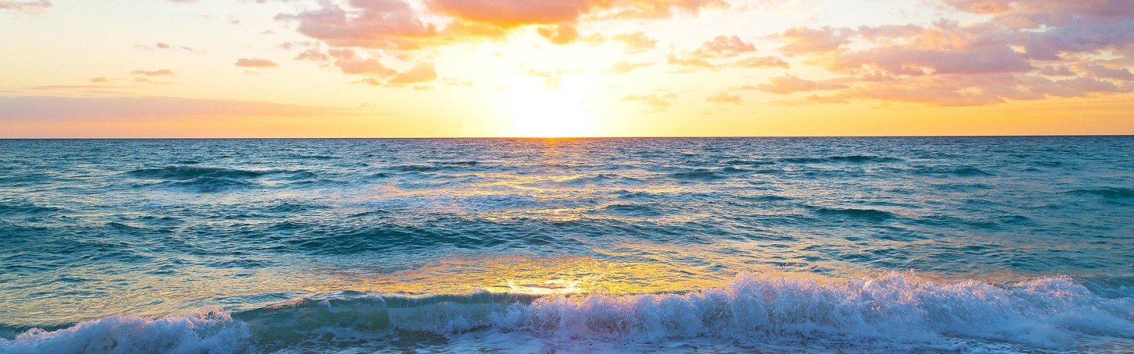 The image shows a beautiful ocean sunset with waves gently crashing onto a sandy beach and clouds scattered across the sky.