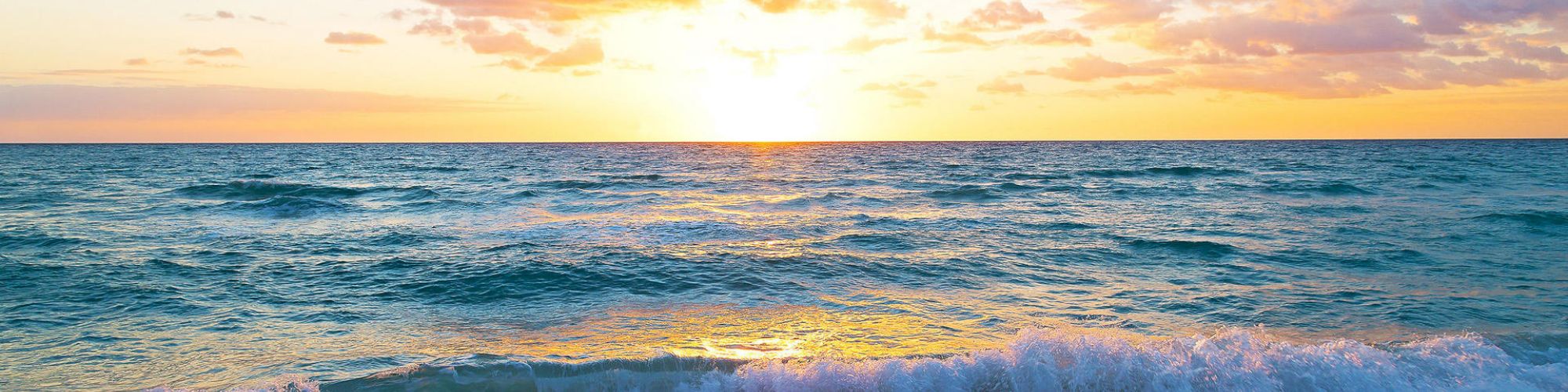 The image shows a beautiful ocean sunset with waves gently crashing onto a sandy beach and clouds scattered across the sky.