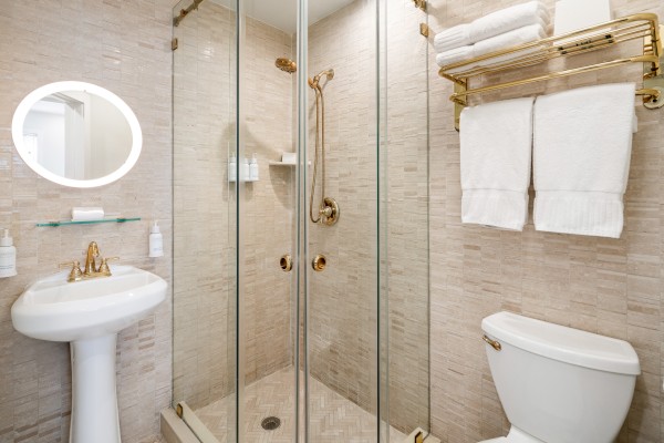 A modern bathroom with a glass shower, white pedestal sink, toilet, and neatly stacked towels on a golden rack.