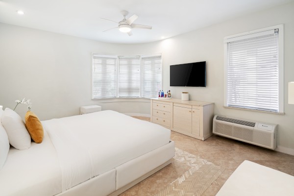 A modern bedroom with a large bed, beige furniture, a wall-mounted TV, and an air conditioning unit under the window completes the look.