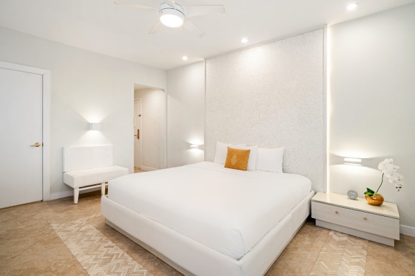 A modern bedroom with a large white bed, flanked by nightstands and decorative lighting, featuring minimalistic decor and neutral tones.