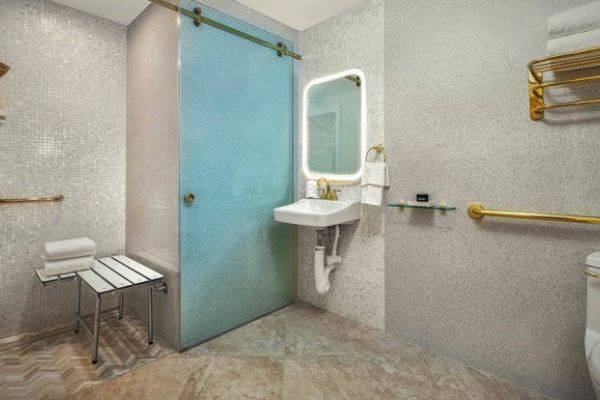 This image shows a modern bathroom with accessible features, including a bench in the shower, grab bars, and a freestanding sink. ADA Guestroom