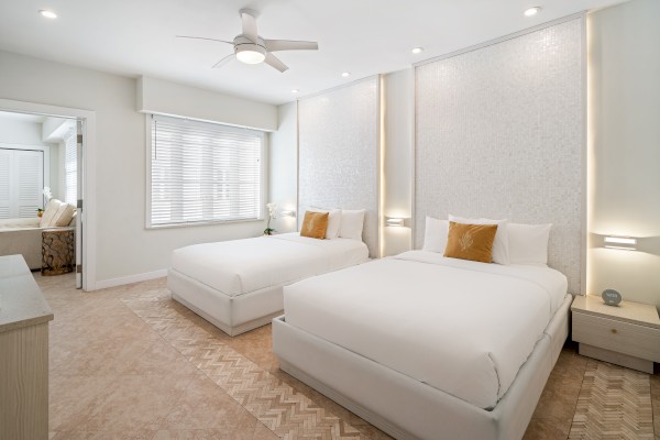 The image shows a modern bedroom with two double beds, white bedding, decorative pillows, nightstands, and a ceiling fan.