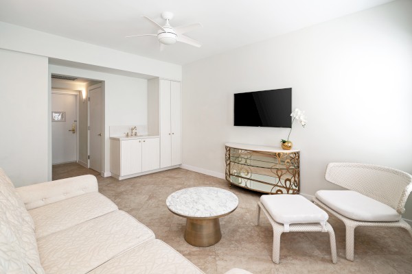 A modern living room with a sofa, marble coffee table, TV on the wall, and white chairs. There's a cabinet and a ceiling fan.