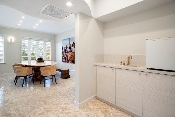 A modern dining area with a round table and chairs. On the right, a kitchenette with a small fridge and sink. Bright, airy, and stylish.