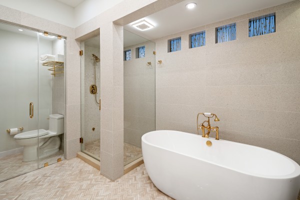 A modern bathroom with a freestanding tub, glass-enclosed shower, toilet, and elegant fixtures. The room has a clean, minimalist design.