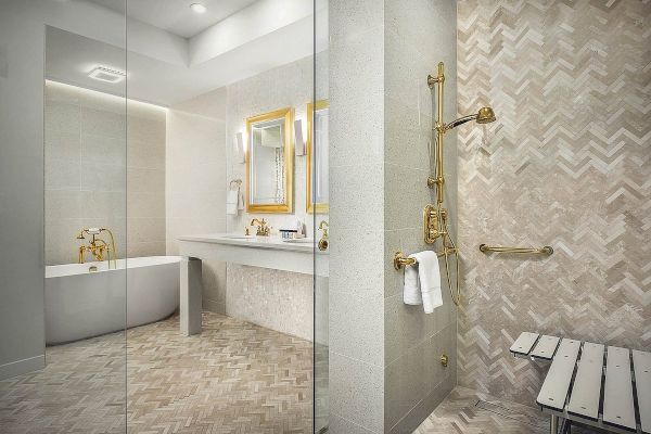 A modern bathroom with herringbone tile, a glass shower, a gold faucet, a standalone bathtub, a double vanity with mirrors, and a stool.