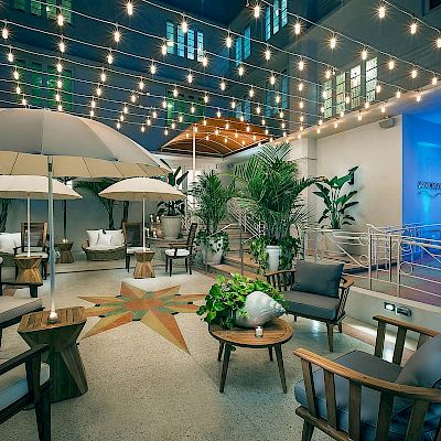 A stylish outdoor patio with string lights, umbrellas, wood furniture, and plants, creating a cozy and inviting atmosphere for relaxation.