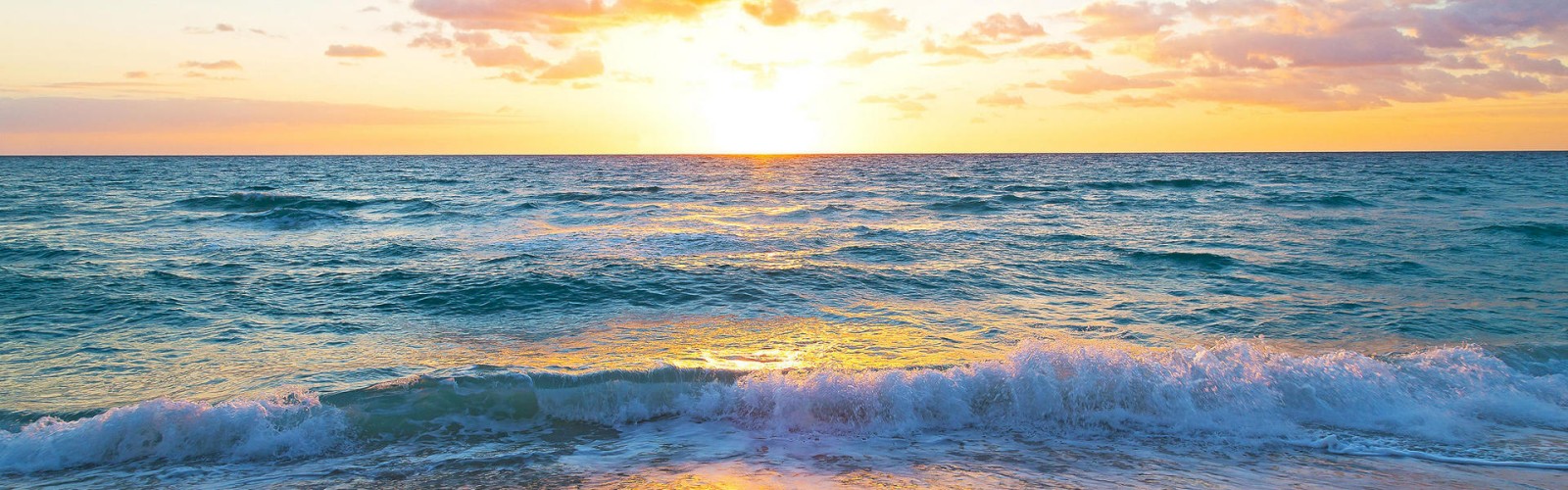 The image shows a sunset over the ocean with waves gently crashing onto a sandy beach, creating a serene and picturesque scene.