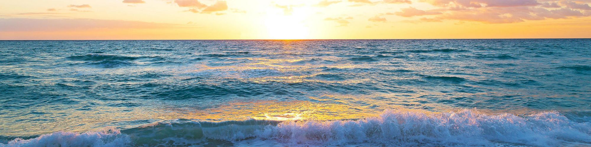The image shows a sunset over the ocean with waves gently crashing onto a sandy beach, creating a serene and picturesque scene.