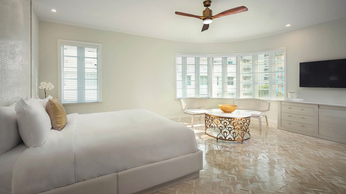 Bright, modern room with sofa, table, fan, TV, and shutters.