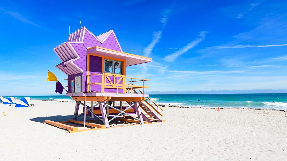 A colorful lifeguard tower on a sunny beach with clear skies and the ocean in the background.