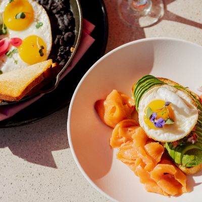 The image shows a meal with sunny-side-up eggs in a pan and a plate with smoked salmon, an avocado, and a poached egg with garnish.