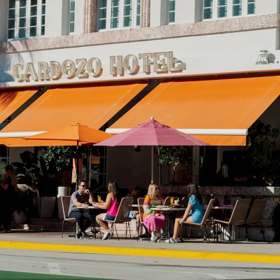 People are sitting at tables under orange awnings outside the Cardozo Hotel.