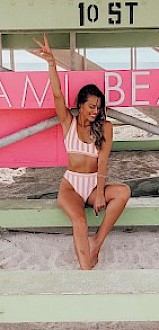 A woman in a striped swimsuit poses under a lifeguard stand with 