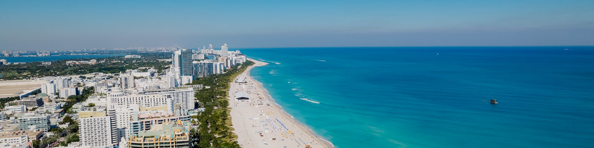 Aerial view of a coastal city with high-rise buildings along a sandy beach, clear turquoise water, and a bright blue sky.