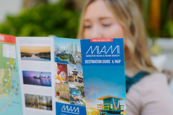 A person is reading a Miami Destination Guide & Map, featuring images and highlights of Greater Miami and Miami Beach.