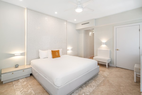 A modern bedroom with a large bed, white bedding, side tables, a rug, and minimal decor in neutral tones.