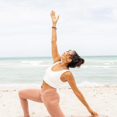 A woman practicing yoga on the beach, in a low lunge pose with one arm raised, enjoying a serene moment by the sea.
